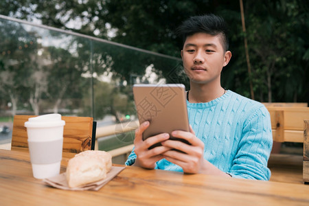 年轻亚洲人坐在咖啡店时使用数码平板电脑的肖像图片