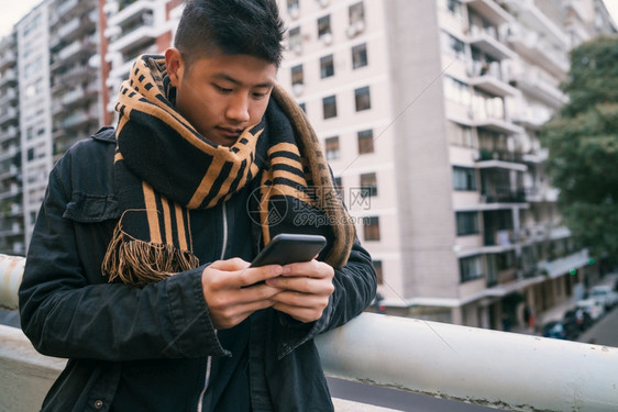 年轻亚洲人使用手机在街上户外站立的肖像图片