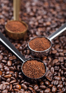 黑银和金钢勺上咖啡豆方的黑银和金钢勺中的新鲜有机咖啡粉背景图片