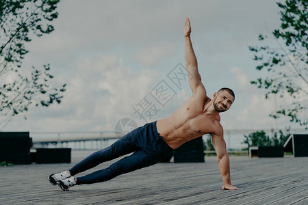健壮的男子站在腹边木板上抬起手臂在户外锻炼有肌肉的身体和快乐表情英俊运动员在露天列车男沙发平衡在手运动概念图片