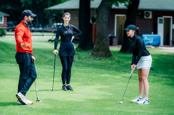 两个年轻女高尔夫运动员练习与高尔夫教一起打高尔夫图片