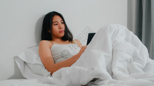 年轻女使用智能手机检查社交媒体感到快乐的笑容早上醒来后躺在床图片