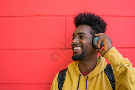 年轻人听音乐时用耳机在红色背景下播放的画像图片