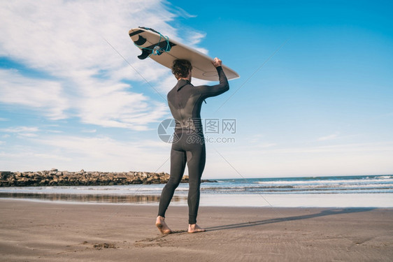 海滩上年轻冲浪手的肖像举起他冲浪板穿着黑色冲浪西装运动和水上的概念图片