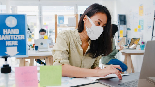 作为商业女企家身戴医疗面罩在新的正常情况下在预防方面保持社会偏移同时在办公室工作使用笔记本电脑在科罗纳后生活和工作图片