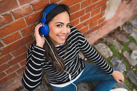 年轻美女在街上户外聆听蓝耳机音乐的肖像图片
