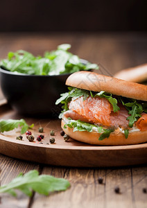 配有鲑鱼和面包圈奶油酪和木本底板上的野生火箭新鲜健康有机三明治图片