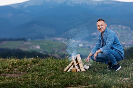 坐在火边的快乐游客在火烟中微笑的旅行者游客在山上抽烟有选择的焦点游客在山上抽烟有选择的焦点图片