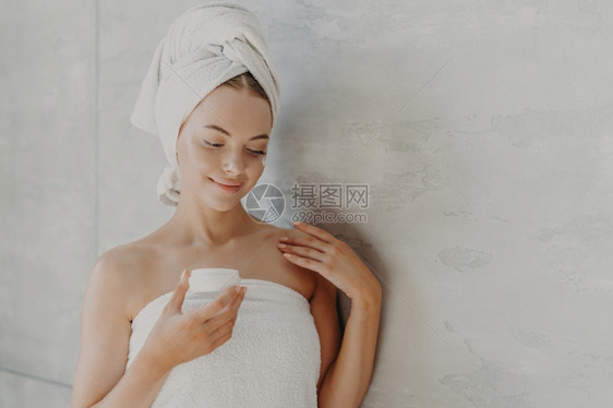 穿着健康皮肤的美容女人最起码的化妆品涂面霜淋浴后被裹在巾上灰色背景附近图片