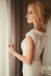 美丽的新娘站在窗边微笑着婚礼那天图片