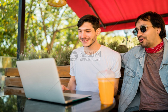 两位年轻朋友在咖啡店户外露宿时使用笔记本电脑的肖像图片