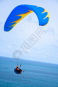 降落伞旅游者享受滑翔运动在蓝海上空高飞背景