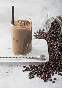 一杯冰咖啡大理石板上加牛奶一罐咖啡豆和勺长子放在浅色桌底图片