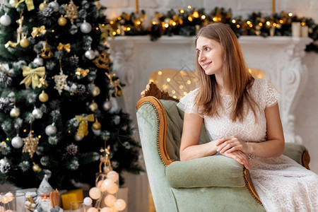 美丽而愉快的黑发女孩带着开放的笑容坐在圣诞树附近的美丽椅子上新一年装饰品假日概念开着微笑的漂亮而愉快黑发女孩坐在圣诞树附近的漂亮图片