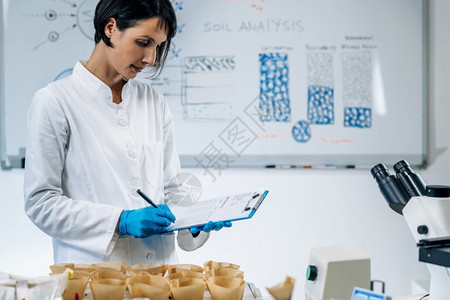 关闭女科学家穿着白色大衣在实验室作笔记的图像图片
