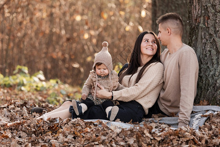 年轻父亲和母与女婴在阳光明媚的日子里在秋天公园的毛毯上放松幸福的家庭概念母亲和父亲和r婴儿和day年轻父亲和母与女婴在阳光明媚的图片