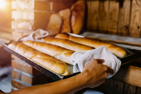 端着烤女面包师握着热烘烤盘和新鲜面包盒的手背景
