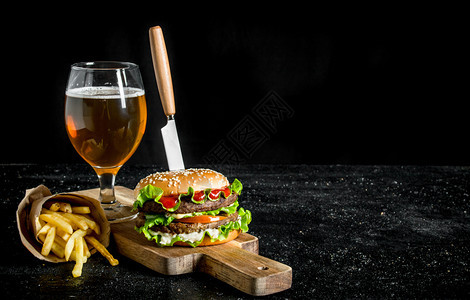 汉堡包用刀子薯条啤酒在杯子里黑色生锈背景啤酒在杯子里图片