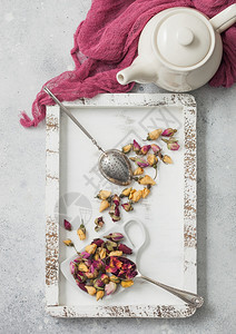 玫瑰花蕾混合木制茶盒叶与古老的训练员infuser和茶壶在白桌背景和红布图片