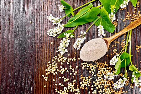 荞麦粉从褐色的谷类调羹中取出花和叶子的背景从上面放在木板上图片