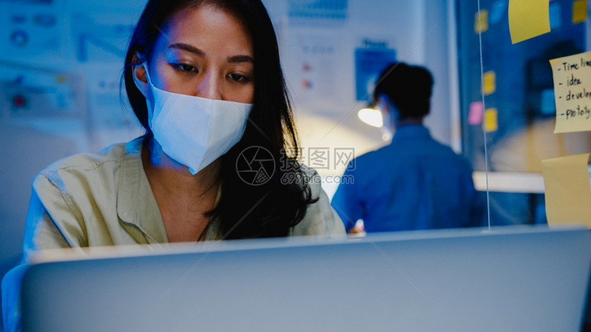 身戴医疗面罩的快乐女商人身着医疗面罩在预防的新正常情况下使用笔记本电脑图片