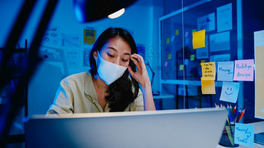 女穿着面罩在新的正常办公室用笔记本电脑做艰苦工作晚上在家超负荷工作与外界隔绝社交不和图片