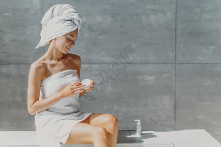 洗完澡后用体液浸润和喂奶油在浴室中用灰墙涂毛巾包着接受美容治疗图片