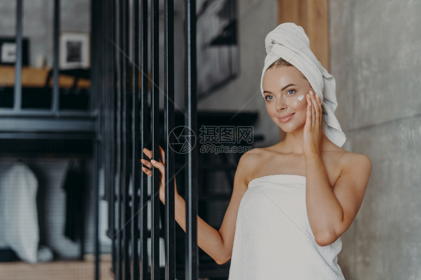 美丽健康的年轻女将面霜涂在外衣上长得像深思熟虑的远处裹着毛巾站在室内拥有完美的纯皮肤女和美容学概念图片