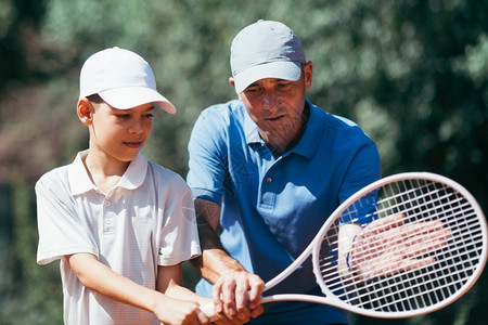 微笑的网球教练男孩如何打网球粘土场上的网球课图片