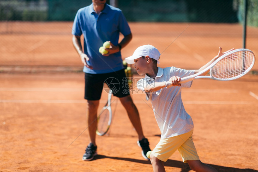 在粘土场上有年轻才华的网球教官有课的男孩在粘土场上与年青男孩一起的网球教官图片
