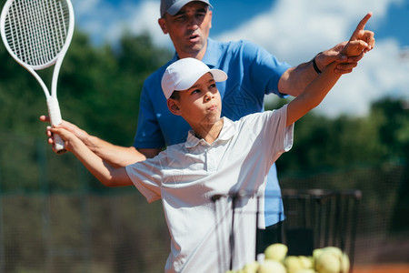 网球教练与男孩一起在网球课室户外与男孩一起练习服务网球教练与初级运动员一起练习服务图片