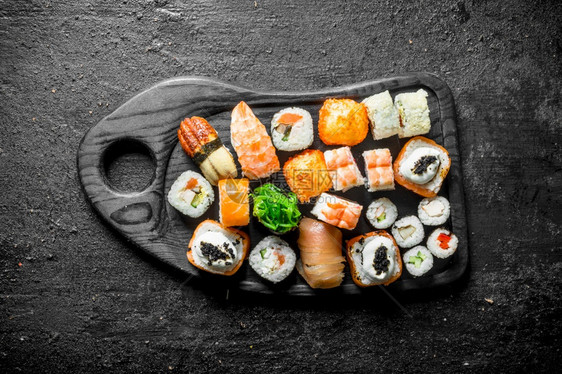 不同的寿司卷在切割板上黑色生锈背景图片
