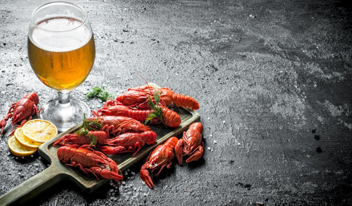 煮熟的龙虾在切口板上面有啤酒和柠檬片黑色生锈背景图片
