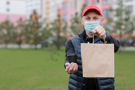 身着红色帽子的送货员面部医疗具紧握着纸袋在市外的一次杯子里喝酒服务科罗纳在线购物图片