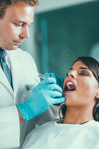 与年轻女病人一起工作的牙医图片