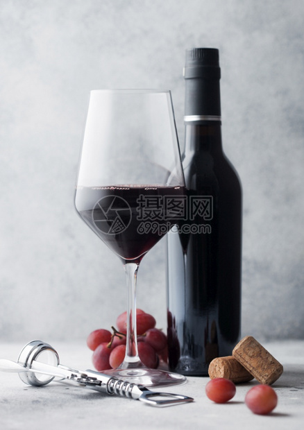 盛有玻璃和软木的红酒小瓶子有钢软木塞和浅色桌底的葡萄图片