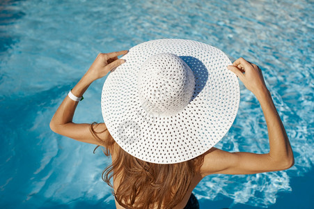 在热带旅行度假胜地的海滩上做日光浴享受暑假女孩在游泳池附近的遮太阳员身上用手戴帽子女孩在游泳池附近的遮太阳员身上戴帽子图片