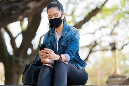 年轻女在户外的楼梯上时戴着面罩并使用手机新的正常生活方式概念城市图片