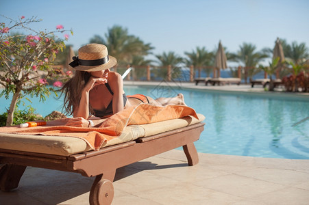 穿着草帽的女子在豪华夏日泳池酒店附近的日睡床上放松概念旅行时间图片