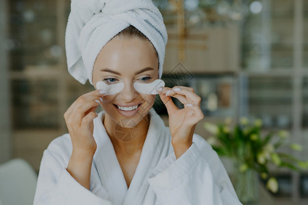 有健康皮肤的快乐年轻女子摘下眼的美容补丁减少皱纹或将毛巾裹在头部上穿着毛巾睡袍面带牙齿的笑容很少化妆图片