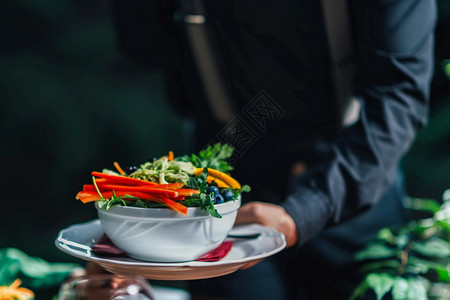 男手在餐厅供应美味素食混合有机沙拉的盘子图片