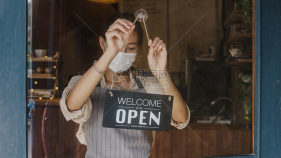 年轻女孩戴着面罩从关上到打开牌子在门外等待关闭后的客户拥有小生意食物和饮料重新开业图片