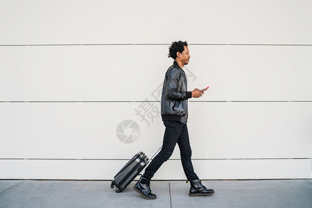 旅游观光客在街上户外行走时使用手机并携带提箱的肖像图片