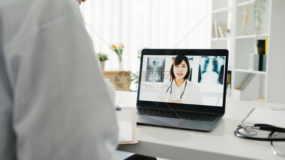 白制服的年轻女医生使用笔记本电脑交谈视频话在诊所或医院的书桌与高级医生交谈社会偏移冠状隔离图片