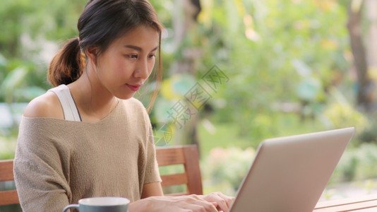 在家工作的女自由职业者早上在花园的桌用笔记本电脑工作的女商人在家里工作的妇女生活方式概念图片