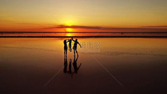 三个爸妈和小女儿的休眠在红色日落的背景下穿过湖浅处三个妈和小女儿的休睡在红色日落的背景下穿过湖浅处图片