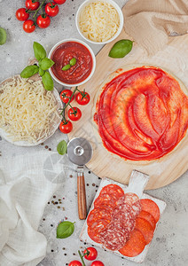 准备用生面粉烤番茄比萨饼沙拉米辣焦索切轮机新鲜西红柿和浅桌上的烤肉碗盘配奶酪和番茄糊图片