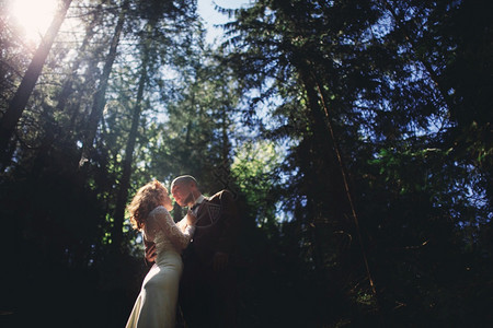 穿着长白色礼服的新娘和穿红色西装的新郎正在拥抱结婚日夏天在绿树林里有漂亮的新婚夫妇在快乐婚礼日图片