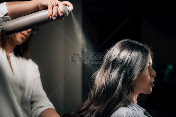 喷洒妇女长黑色头发的型喷雾在沙龙里图片