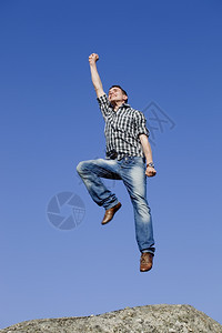 年轻快乐的男孩跳跃在岩石顶上图片